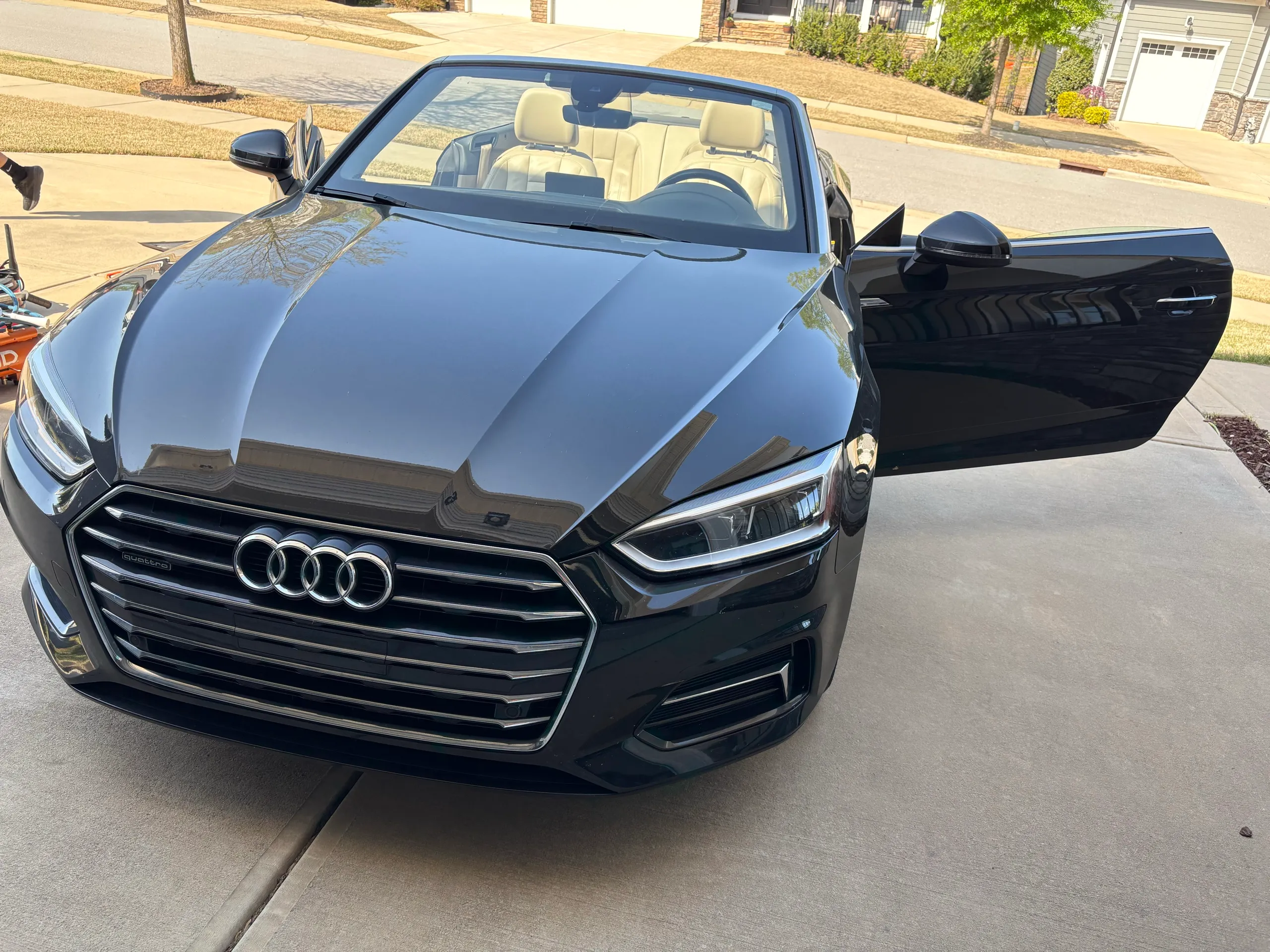 Black Audi A5 Cabriolet with top down and driver door open, showing freshly detailed exterior and cream leather interior