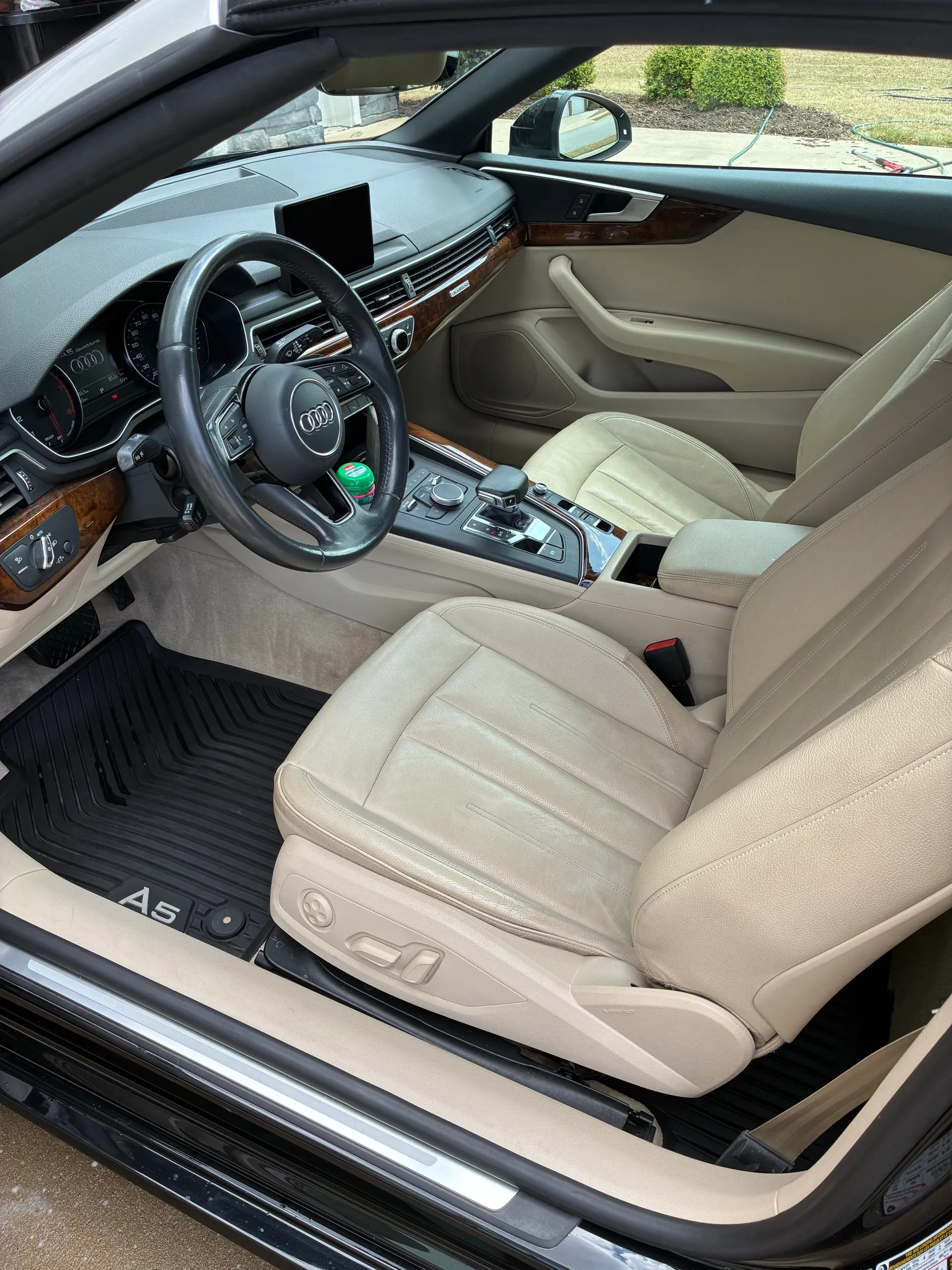 Cream leather driver seat and dashboard of an Audi A5, with the A5 logo embroidered on the floor mat